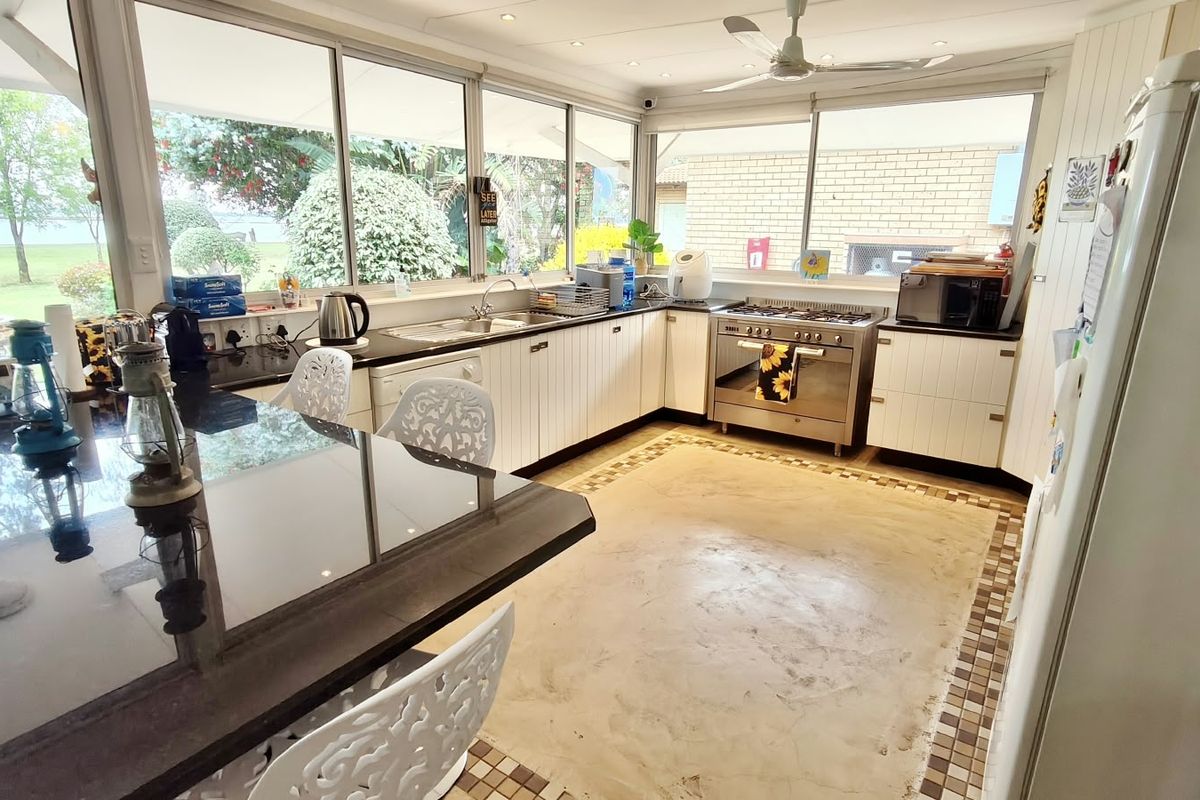 Spacious kitchen featuring stainless steel appliances, ample cabinetry, a breakfast bar, and large windows overlooking the garden, with potential for floor updates.
