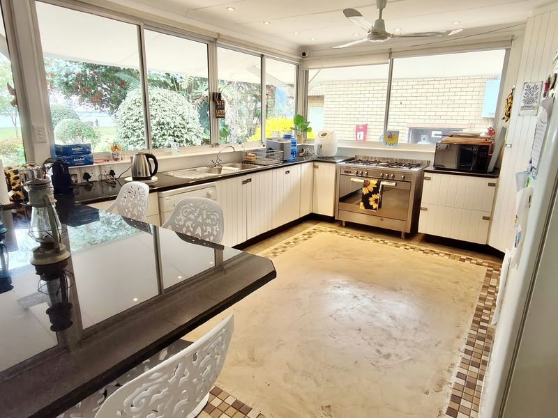 Spacious kitchen featuring stainless steel appliances, ample cabinetry, a breakfast bar, and large windows overlooking the garden, with potential for floor updates.