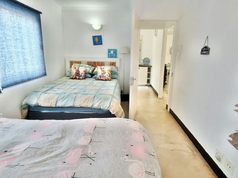 A bedroom featuring concrete flooring and roller blinds, with an adjacent hallway visible through the doorway.