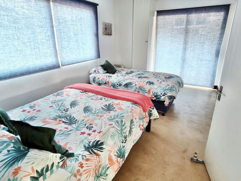 A bedroom featuring concrete flooring, large windows with roller blinds, and a sliding glass door providing natural light.