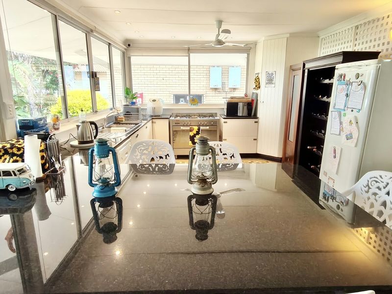 Bright kitchen featuring a large granite island, stainless steel gas stove, and extensive windows overlooking the garden area.