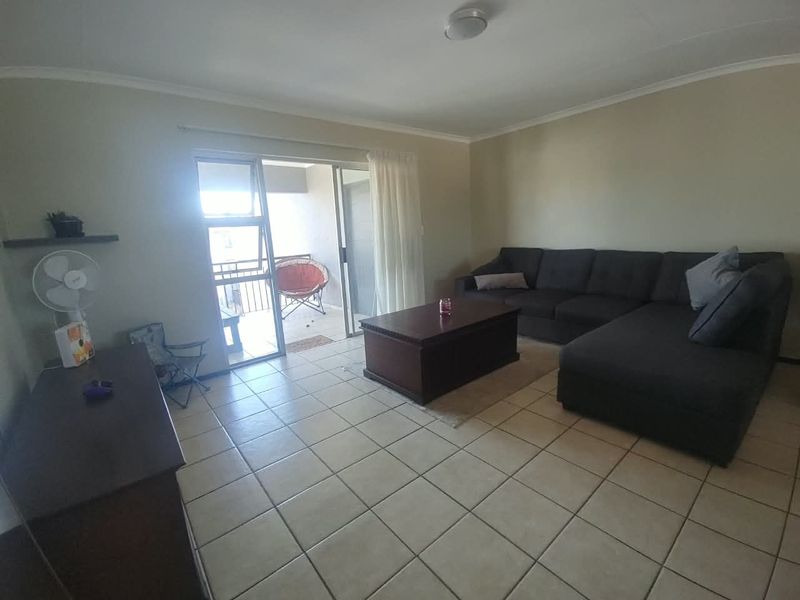 A spacious living room featuring neutral tiled flooring and a large sliding glass door that provides access to an attached balcony.