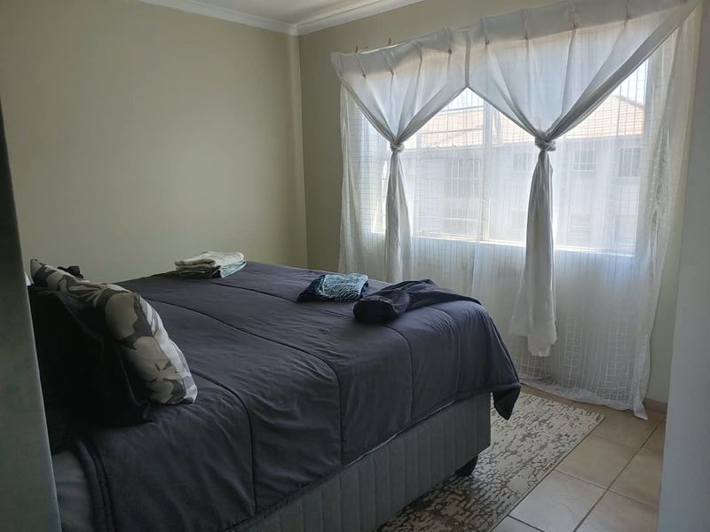 A functional bedroom featuring tiled flooring, neutral wall finishes, and a large window allowing for natural light.