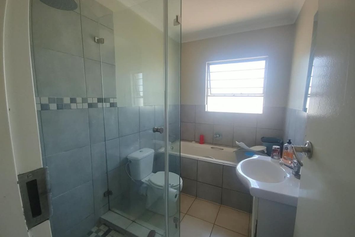 A functional bathroom featuring a glass-enclosed shower, a built-in bathtub, a pedestal basin, and tiled finishes throughout.