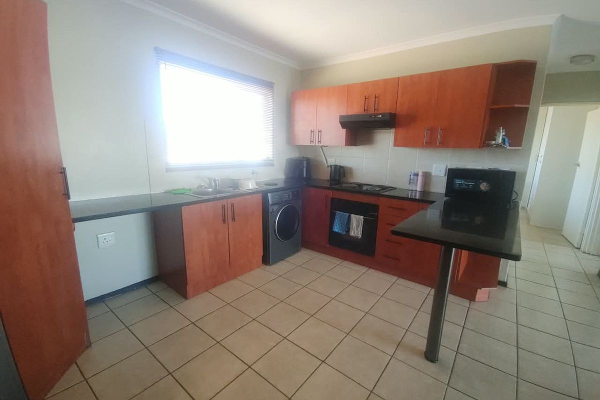 A functional kitchen featuring wood-finish cabinetry, granite countertops, integrated oven and hob, and tiled flooring with a breakfast bar extension.