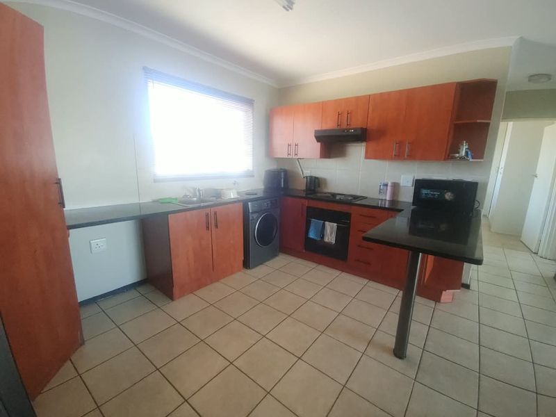 A functional kitchen featuring wood-finish cabinetry, granite countertops, integrated oven and hob, and tiled flooring with a breakfast bar extension.