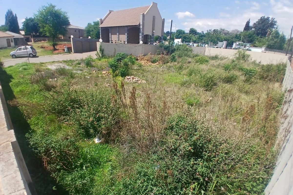A vacant residential plot featuring overgrown vegetation and enclosed by perimeter boundary walls in a suburban neighborhood setting.