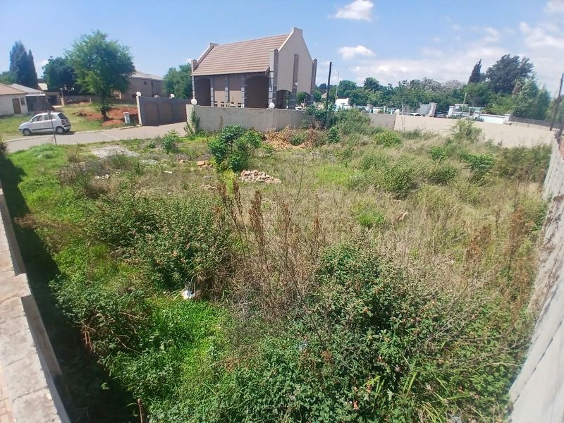 A vacant residential plot featuring overgrown vegetation and enclosed by perimeter boundary walls in a suburban neighborhood setting.