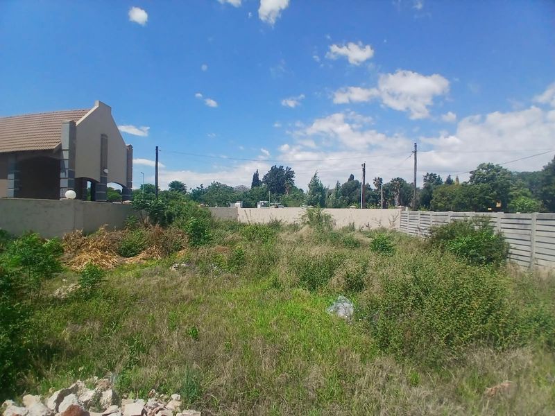 A vacant residential plot featuring overgrown vegetation and enclosed by perimeter walling and precast concrete fencing.