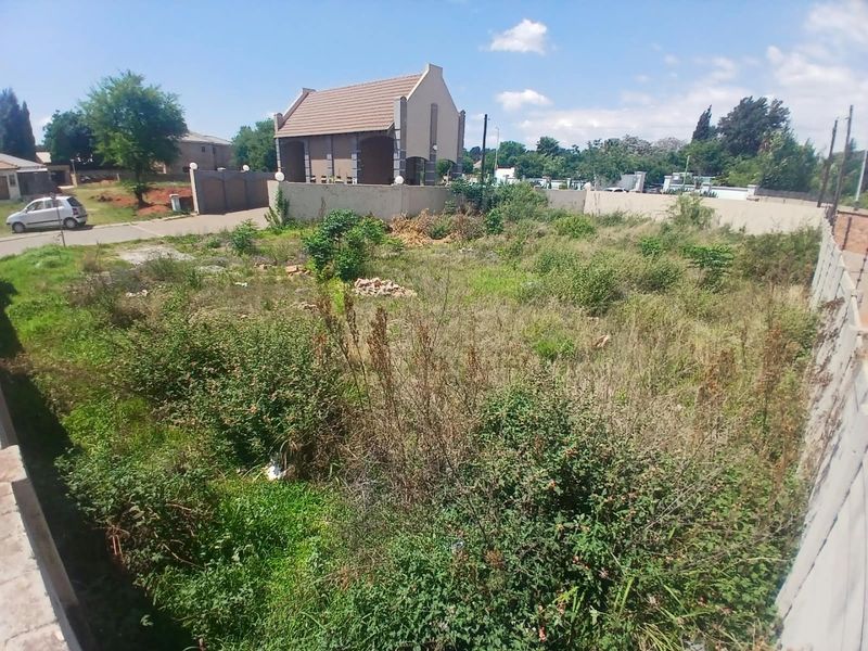Vacant residential land plot featuring perimeter walling and established vegetation, offering a clear space for future development in a residential area.