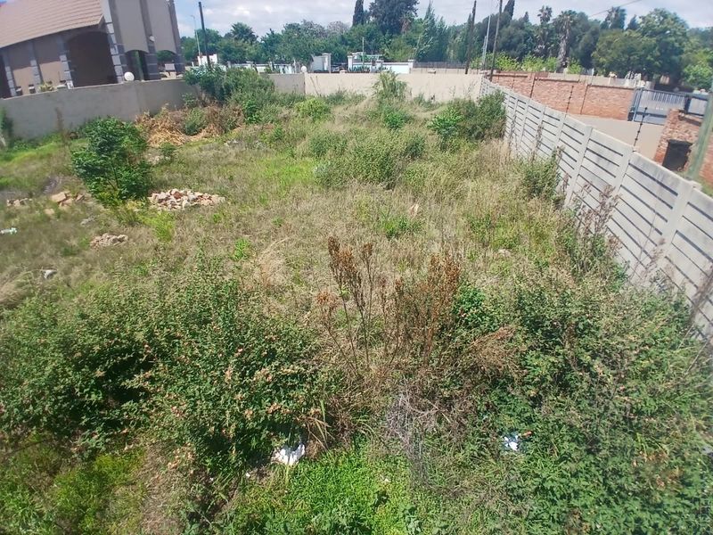 A vacant residential plot featuring overgrown vegetation and enclosed by precast concrete and brick boundary walls.