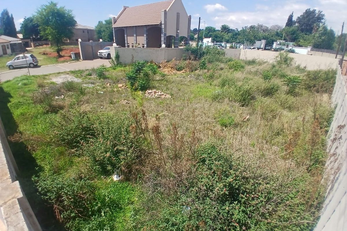 A vacant residential plot featuring perimeter walling and boundary fencing, currently covered in overgrown vegetation.