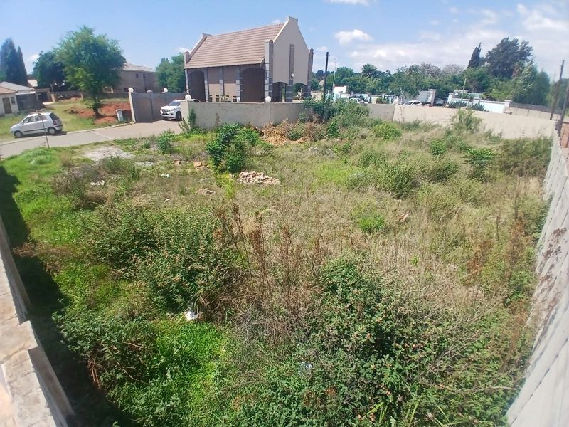 A vacant residential plot featuring perimeter walling and boundary fencing, currently covered in overgrown vegetation.