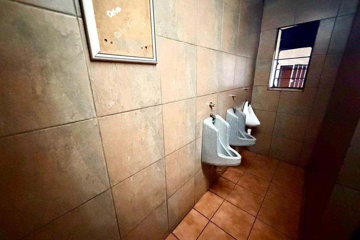 A commercial restroom facility featuring wall-mounted urinals, tiled walls and flooring, and a window with security bars.