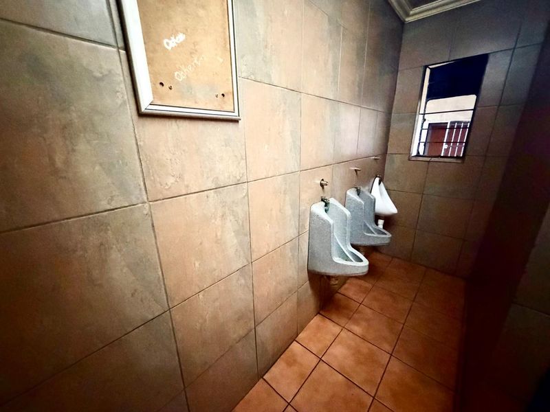 A commercial restroom facility featuring wall-mounted urinals, tiled walls and flooring, and a window with security bars.