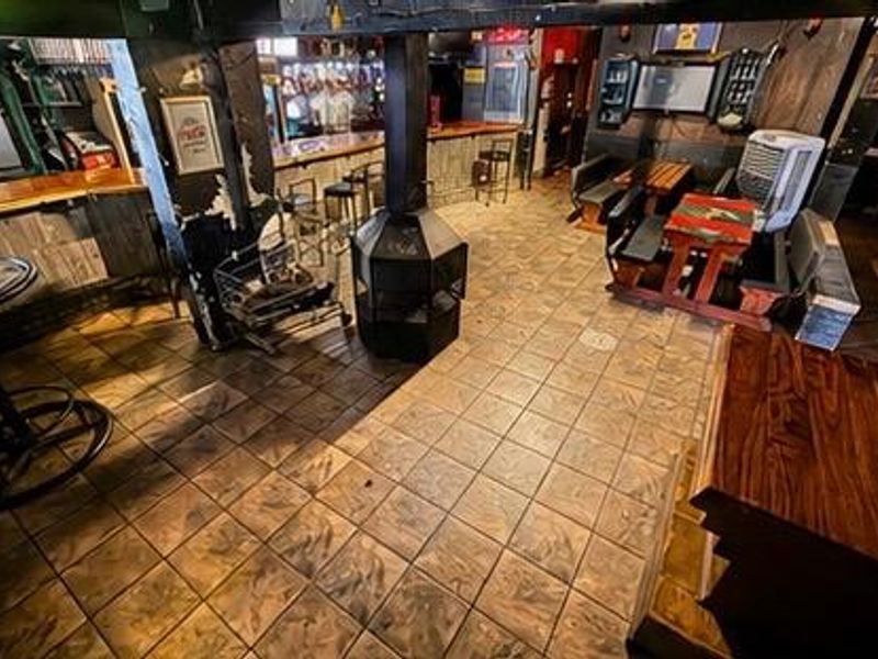 A commercial bar area featuring a built-in counter, tiled flooring, and a central fireplace, showing signs of wear and dated finishes.