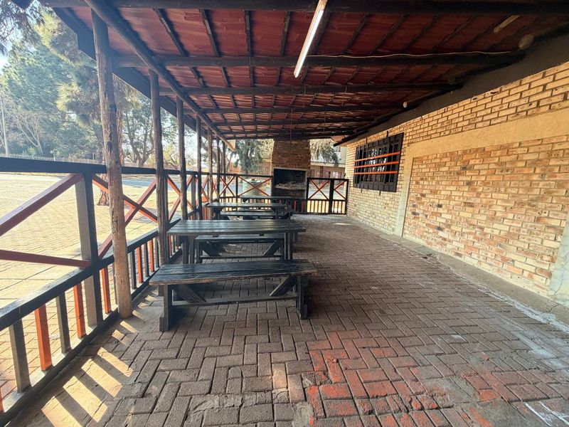 Covered outdoor patio area featuring brick paving, an exposed timber roof structure, and a built-in braai, suitable for commercial entertainment or dining use.