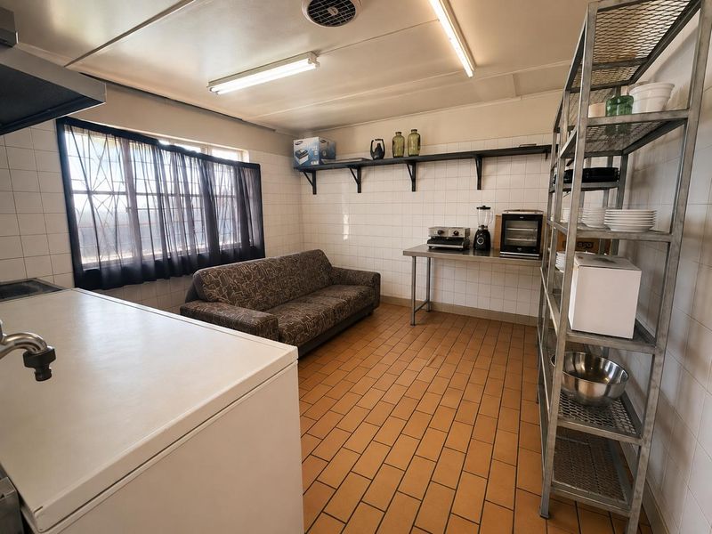 A functional commercial kitchen space featuring tiled walls and flooring, fluorescent lighting, and wall-mounted shelving, suitable for food preparation or utility use.