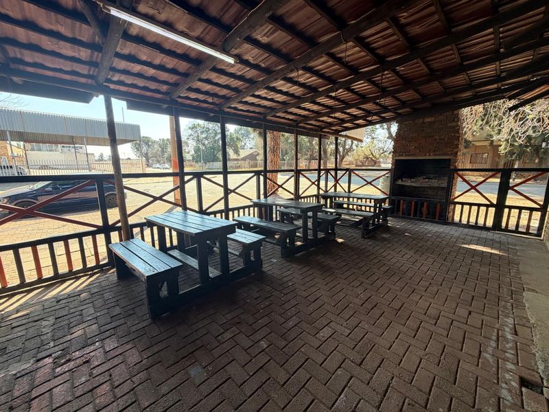 Covered outdoor patio area featuring brick paving, a built-in brick fireplace, and timber roof structure, suitable for commercial entertainment or break-out space.
