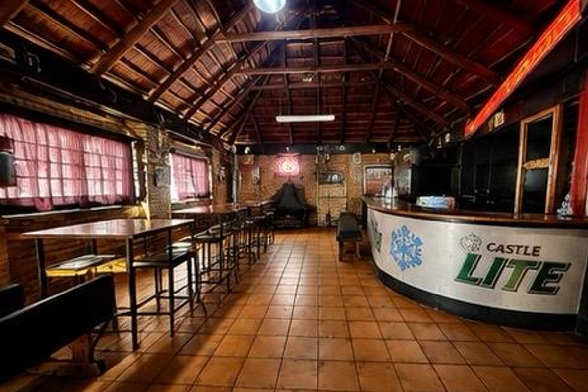 A spacious commercial bar area featuring a large built-in counter, exposed timber roof trusses, and tiled flooring, suitable for hospitality or entertainment use.