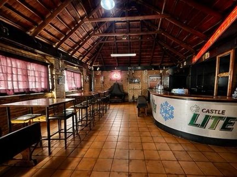 A spacious commercial bar area featuring a large built-in counter, exposed timber roof trusses, and tiled flooring, suitable for hospitality or entertainment use.