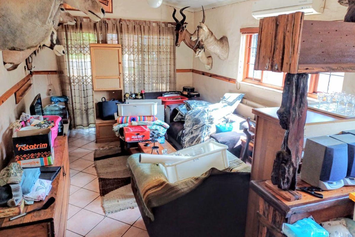 A living room featuring tiled flooring, a ceiling fan, and a wall-mounted air conditioning unit, currently cluttered with personal items.