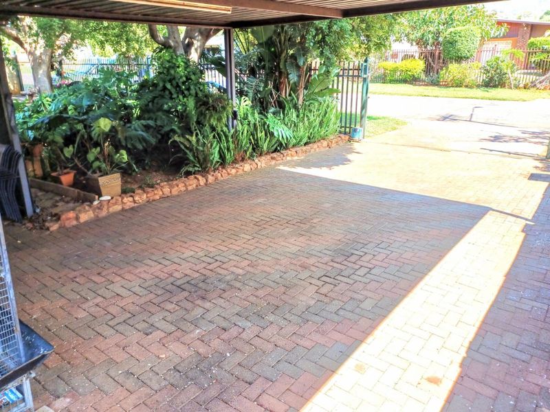 A covered carport area featuring durable brick paving and a secure metal gate, surrounded by established garden landscaping.