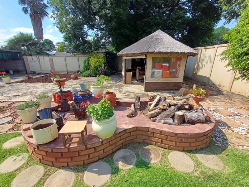 Spacious garden featuring a traditional thatched lapa, a built-in brick fire pit, and paved outdoor entertainment areas, offering potential for landscaping improvements.