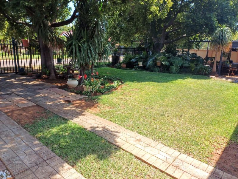 A well-established garden featuring a paved walkway, mature trees, and perimeter metal fencing, providing a private and green outdoor space.