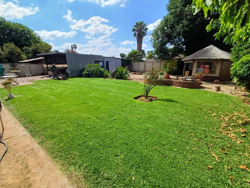Spacious backyard featuring a well-maintained lawn, a traditional thatched lapa, and a paved outdoor entertainment area.