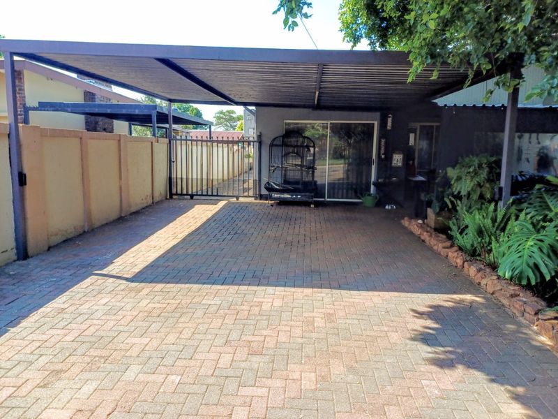 A paved driveway featuring a covered carport, secure metal gate, and boundary wall, providing convenient off-street parking and access to the home.