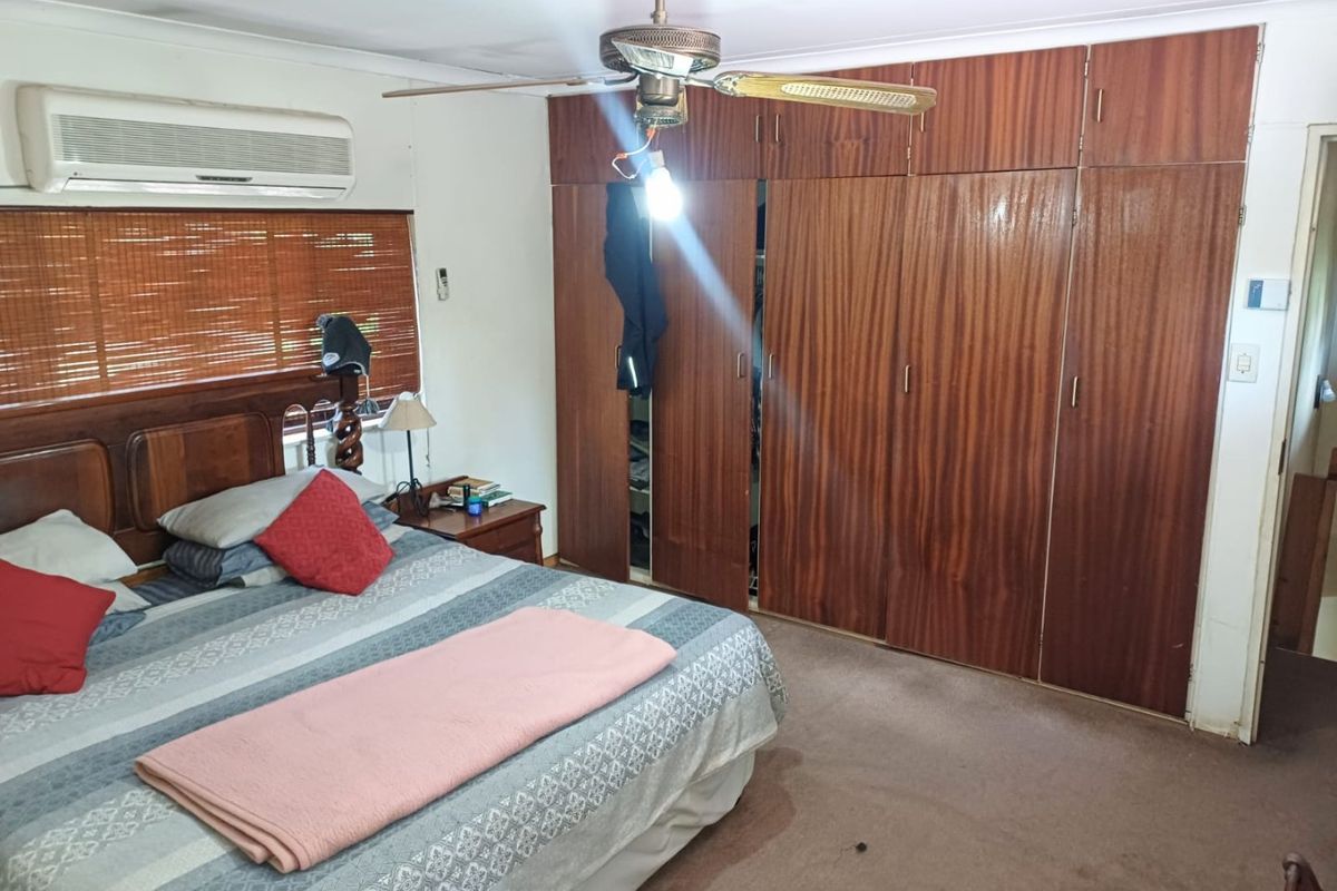Bedroom featuring built-in wooden wardrobes, wall-mounted air conditioning, and a ceiling fan. The space would benefit from cosmetic updates to finishes and flooring.