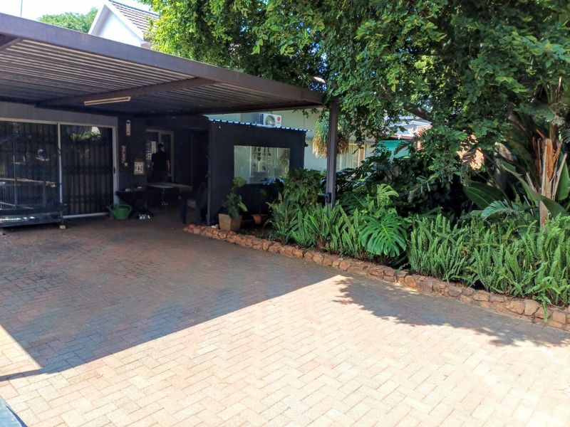 A paved driveway leading to a covered carport area with established garden landscaping and stone edging.