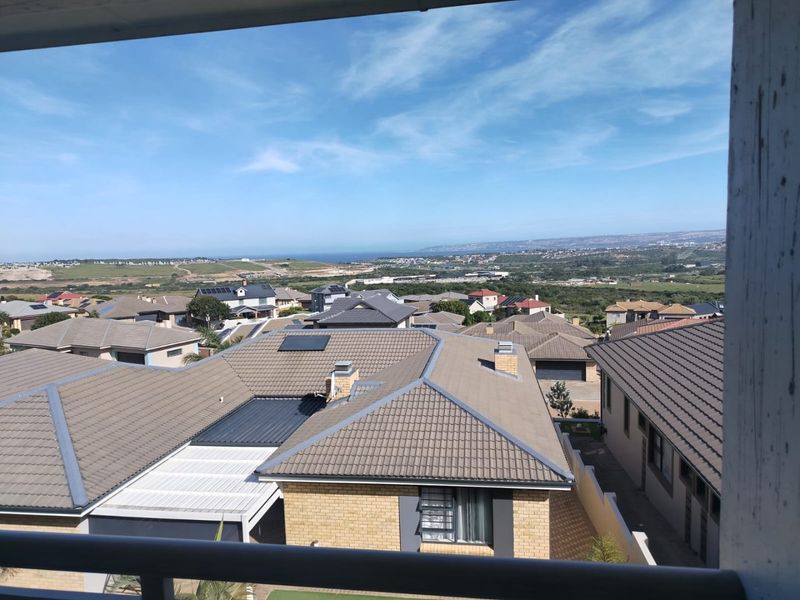 Elevated panoramic view overlooking a residential neighborhood with distant coastal scenery, captured from a balcony.