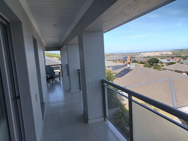 A spacious covered balcony featuring tiled flooring, a modern glass balustrade, and recessed ceiling lighting, offering elevated views of the surrounding neighborhood.