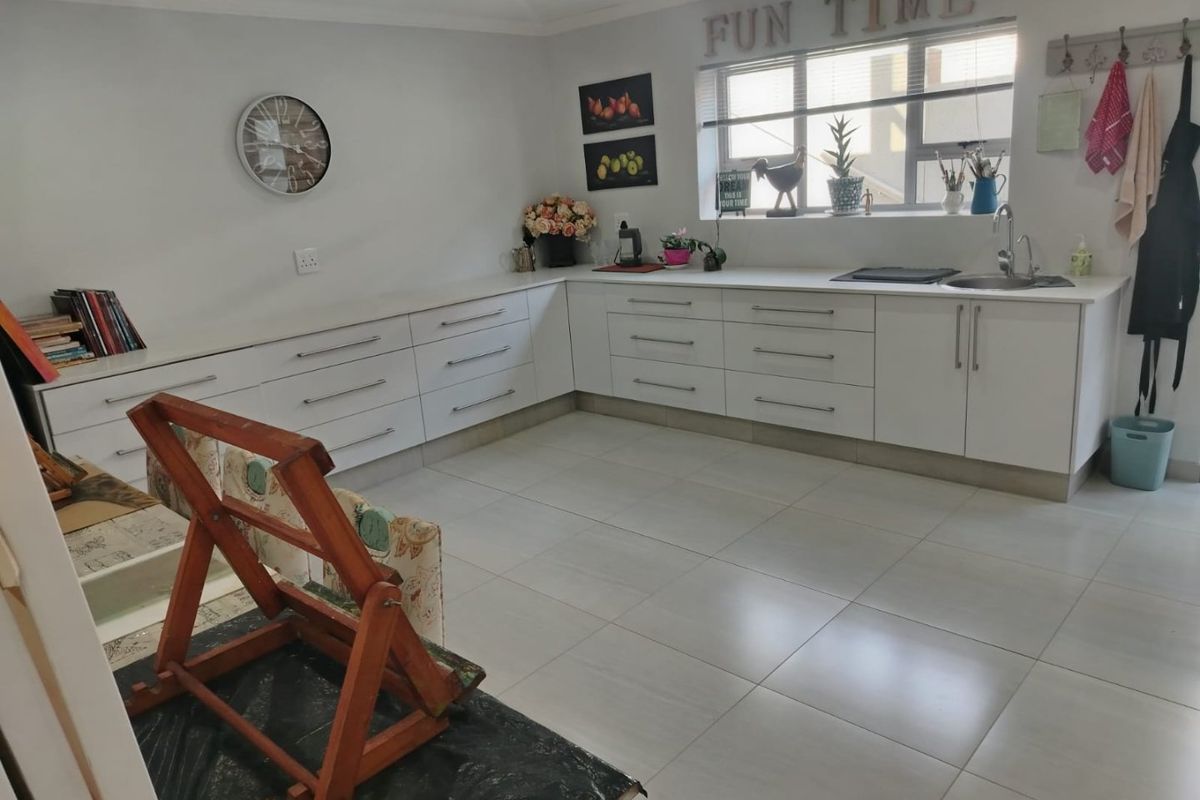 A clean, modern kitchen featuring white cabinetry, ample counter space, tiled flooring, and a functional sink area with natural light.