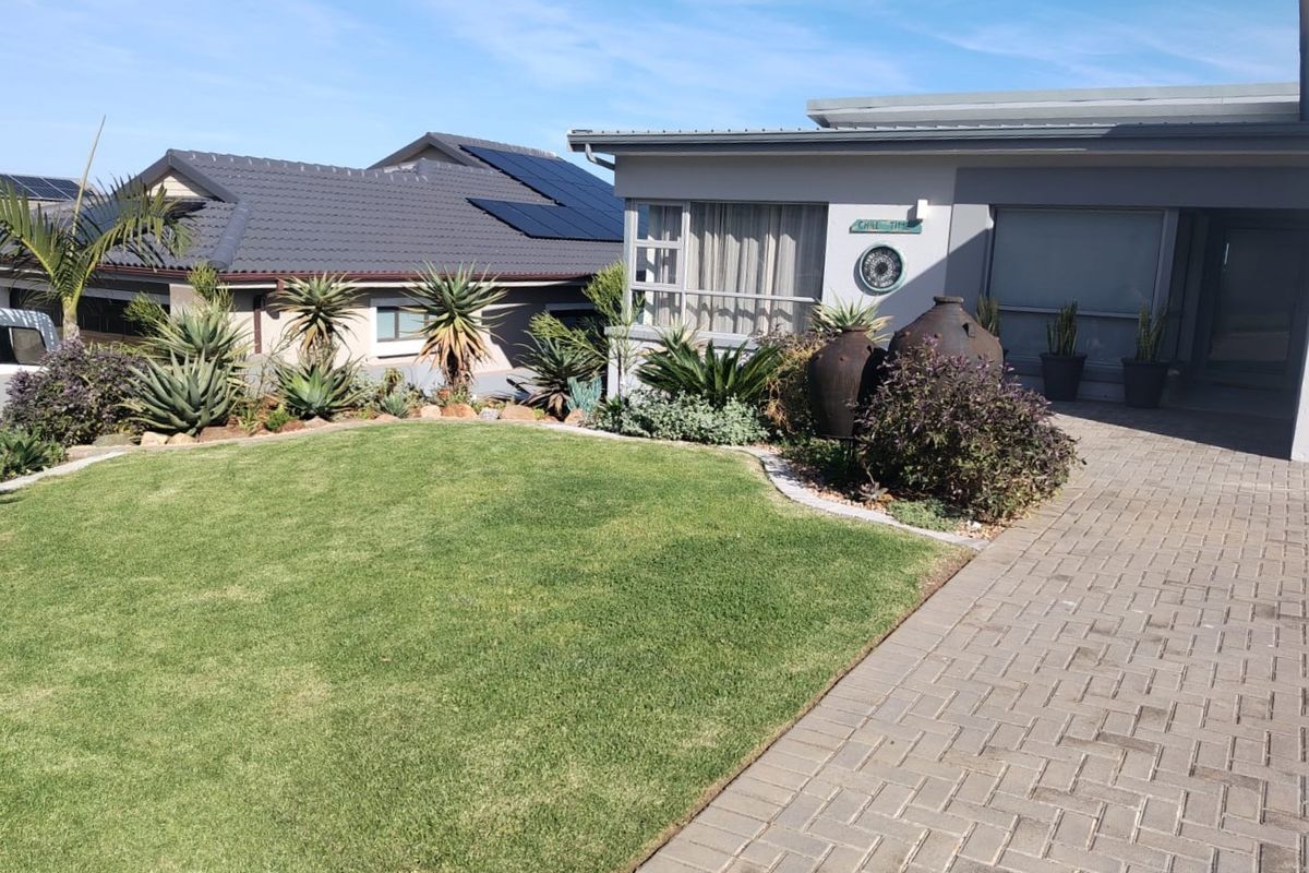 A well-maintained front exterior featuring a paved driveway, manicured lawn, and landscaped garden beds with a modern tiled roof and solar panels.