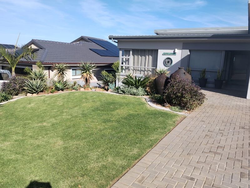 A well-maintained front exterior featuring a paved driveway, manicured lawn, and landscaped garden beds with a modern tiled roof and solar panels.