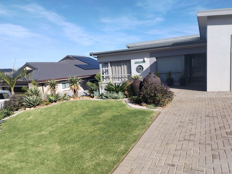 Front view of a modern house featuring a paved driveway, well-maintained lawn, landscaped garden, and solar panels on the roof.