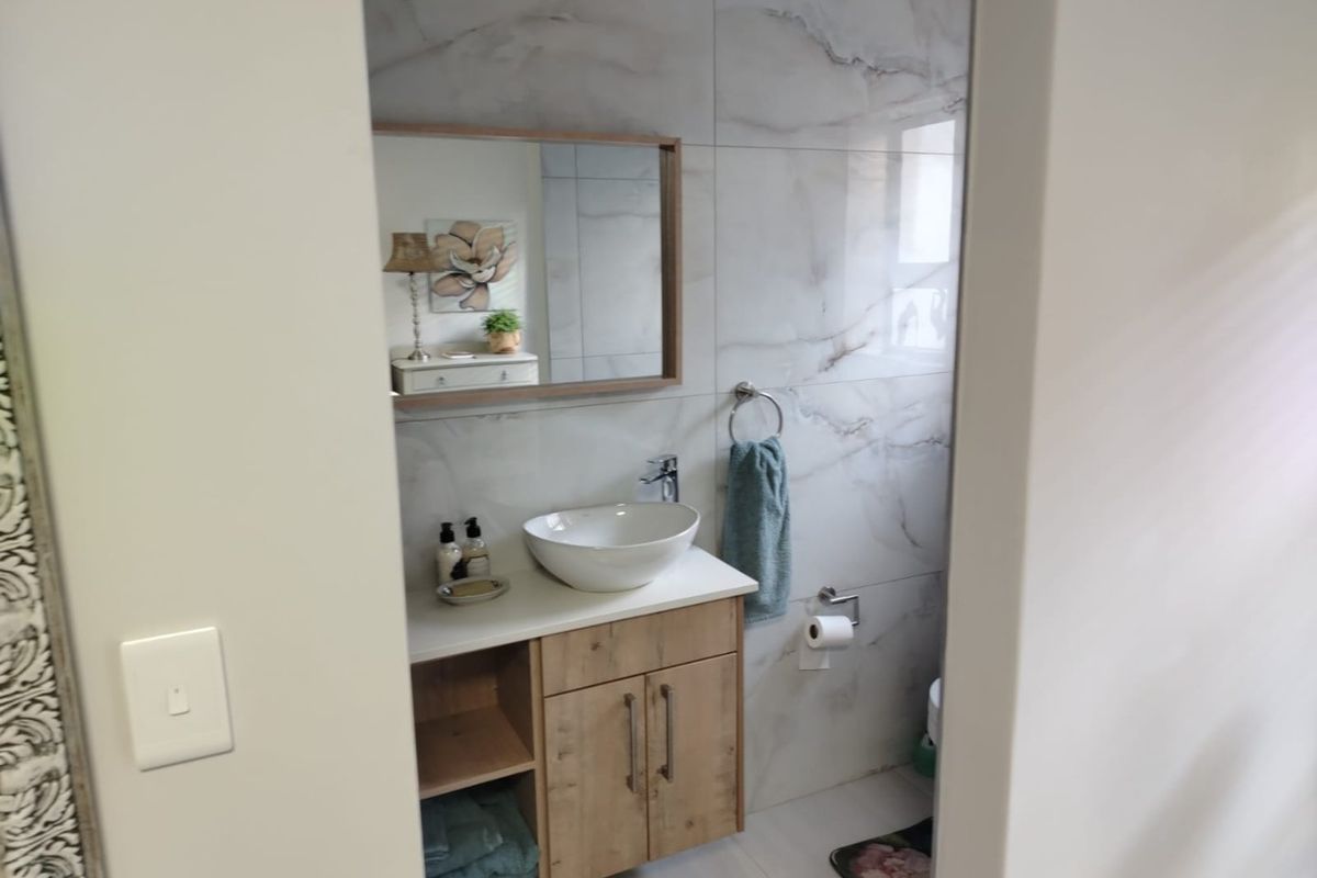 A modern bathroom featuring a vessel sink on a wooden vanity cabinet, complemented by elegant marble-look wall tiles and a framed mirror.