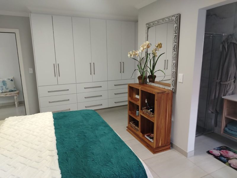Spacious bedroom featuring extensive built-in cupboards, neutral tiled flooring, and direct access to an en-suite bathroom.