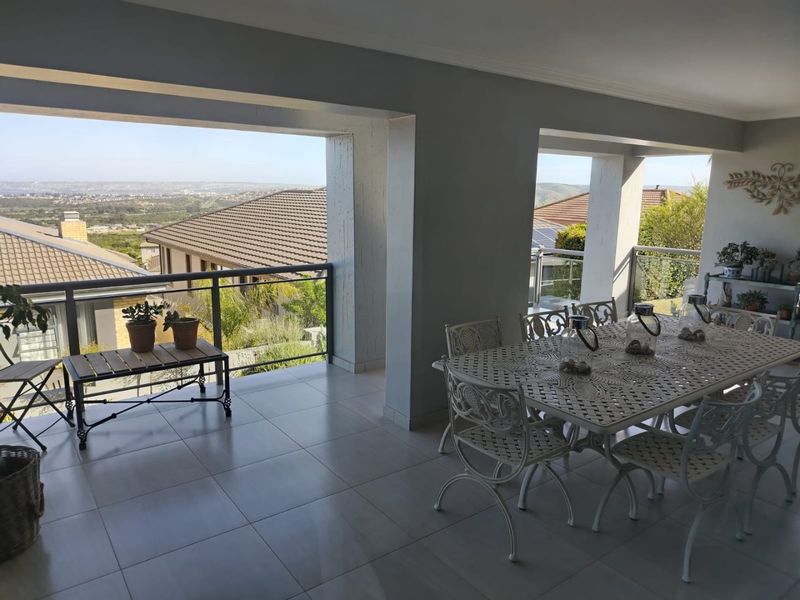 A spacious covered patio featuring tiled flooring and a glass balustrade, offering expansive elevated views of the surrounding neighborhood and landscape.