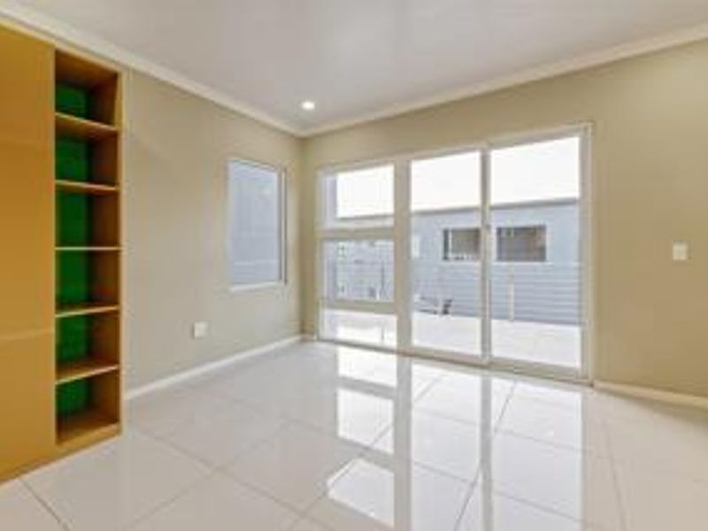 A bright, empty bedroom featuring modern tiled flooring, built-in cupboards with open shelving, and a large sliding glass door leading to an outdoor area.