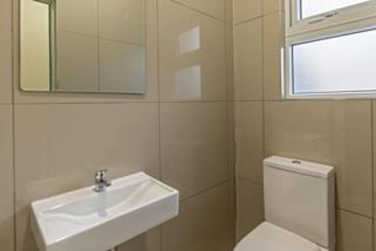 A clean and modern bathroom featuring tiled walls, a wall-mounted basin with a chrome mixer tap, a toilet, and a frosted glass window.