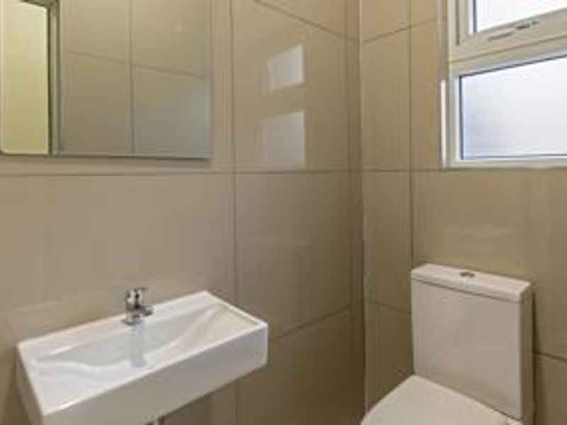 A clean and modern bathroom featuring tiled walls, a wall-mounted basin with a chrome mixer tap, a toilet, and a frosted glass window.