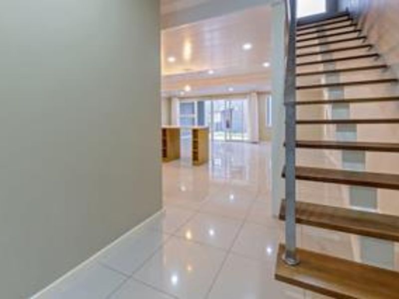 Spacious open-plan living area featuring modern tiled floors, recessed lighting, and a contemporary open staircase with a metal balustrade leading to the upper level.