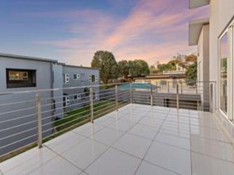A spacious, modern balcony featuring white tiled flooring and a sleek stainless steel balustrade, offering an open outdoor area accessible via sliding glass doors.