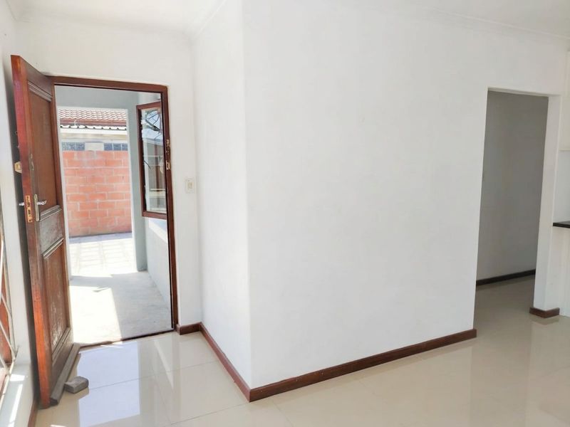 An empty, neutrally painted living area featuring tiled flooring, timber skirting boards, and a wooden door leading to an outdoor space.