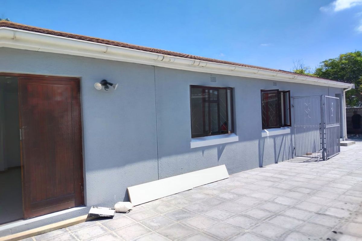 Rear exterior view of the property featuring a paved patio area, security gate, and external wall lighting.