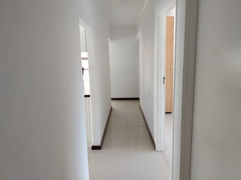 A clean, neutral hallway featuring tiled flooring and white walls, providing access to adjacent rooms within the property.